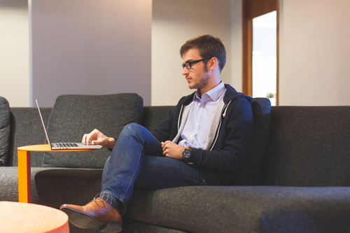 middle aged man sitting on a sofa with his legs crossed and his laptop on a table in front of him