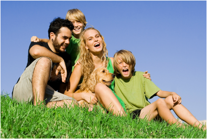 image of a family laughing and sitting on top of a grassy hill